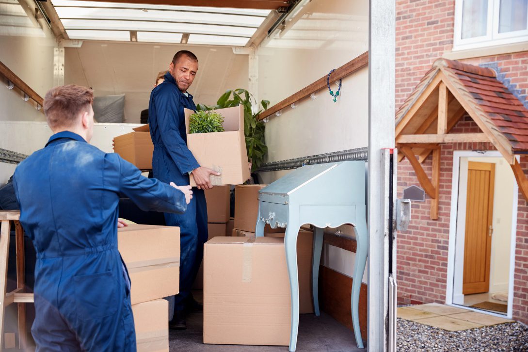 Professional movers loading cardboard boxes and furniture into a moving truck outside a home.