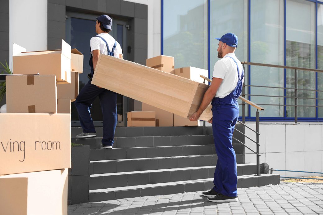 Professional movers carrying furniture and boxes into a home during a residential move.